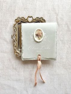 a small brooch sitting on top of a white cloth covered table next to a gold frame