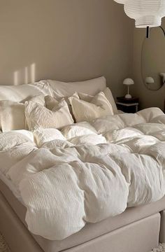 an unmade bed with white sheets and pillows in a small room next to a lamp