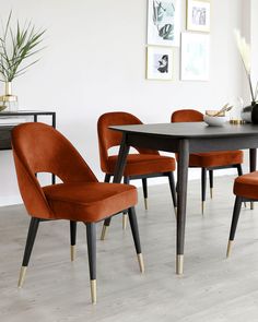 a dining room table and chairs with orange velvet upholstered seats, in front of a white wall