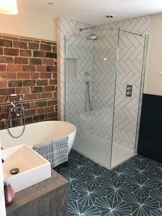 a white bath tub sitting next to a brick wall in a bathroom with blue and white flooring