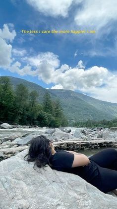 a woman laying on top of a rock next to a river