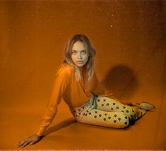 a woman is sitting on the floor with her legs crossed and wearing an orange top