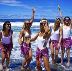 four women in bathing suits are standing in the water at the beach and one is holding her hand up