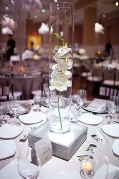 there is a vase with flowers in it on top of a table set for an event