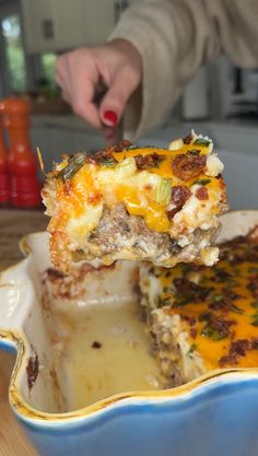 a person is taking a slice of lasagna casserole out of the casserole dish