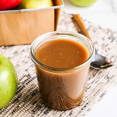 an apple cider next to some apples and cinnamon sticks on a cloth with a spoon