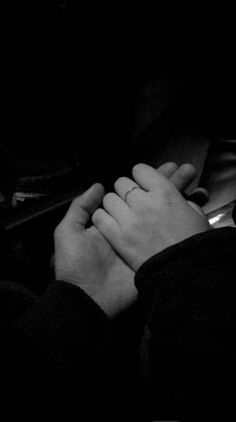 black and white photograph of two hands holding each other in the dark, with one person's arm wrapped around another hand