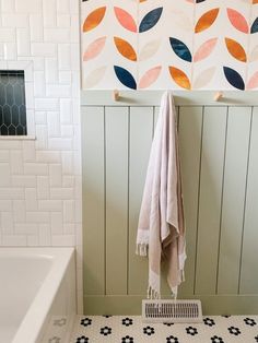 a white bath tub sitting under a window next to a wall mounted towel rack with colorful leaves on it