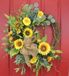 a wreath with sunflowers and greenery hangs on a red door