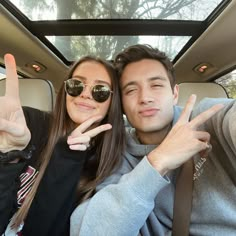 a man and woman sitting in the back seat of a car with their fingers up