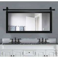 a bathroom vanity with two sinks and a large mirror above it, in front of a gray wall