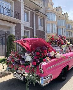 an old pink car with flowers on the hood parked in front of a row of apartment buildings