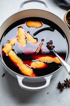 a pot filled with liquid next to spices and star anise on a table top