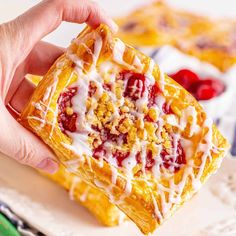 a hand holding a pastry with icing and cranberry toppings on it