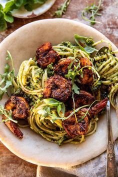 pasta with shrimp and pesto in a white bowl next to silverware on a table