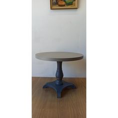 a round table sitting on top of a wooden floor next to a painting hanging on the wall