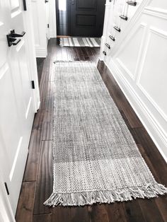 a hallway with white walls and wooden floors has a rug on the floor that looks like woven fabric