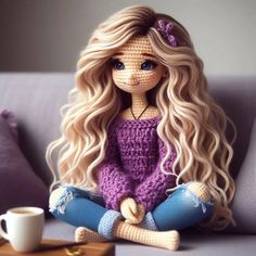 a crocheted doll sitting on top of a couch next to a coffee cup