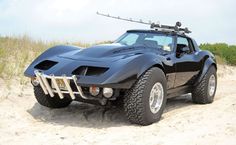 a black car parked on top of a sandy beach next to grass and sand dunes