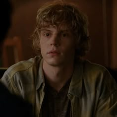 a young man with curly hair sitting in front of a mirror looking at another person