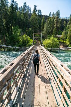 a woman walking across a wooden bridge over a river