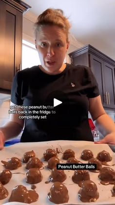 a woman standing in front of a baking tray filled with chocolate covered donut holes