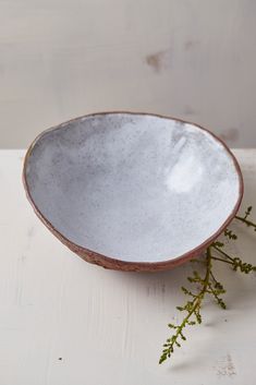 a white and brown bowl sitting on top of a table next to some green plants