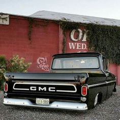 an old black truck parked in front of a red building with graffiti on it's side