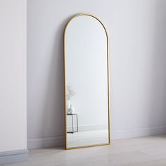 a large mirror sitting on top of a floor next to a white wall with a plant in it