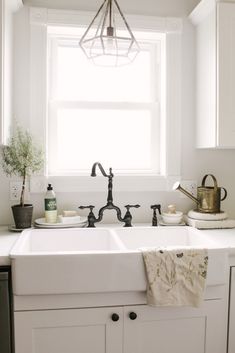 a white kitchen sink sitting under a window next to a potted plant in a vase