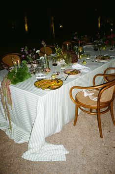 a table set up with food and flowers on it for an outdoor dinner party at night