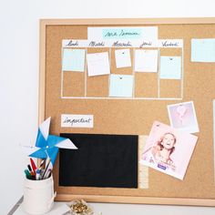 a cork board with pictures, memos and pens on it next to a cup