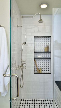 a white tiled bathroom with black and white floor tiles, shower head, and towel rack