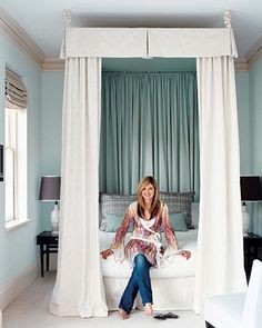 a woman sitting on top of a white bed in a room with green walls and curtains