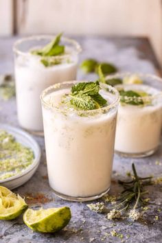 three glasses filled with drinks and garnished with mint leaves on a table next to sliced limes