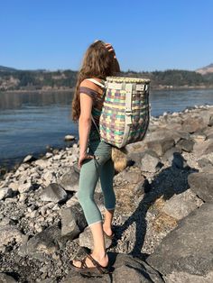 a woman walking on rocks near the water with a large bag in her back pocket