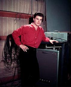 a man in a red shirt standing next to a desk with a hair dryer on it