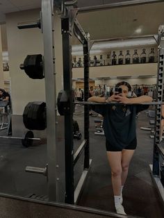 a woman taking a selfie in front of a mirror at the gym with her hands behind her head