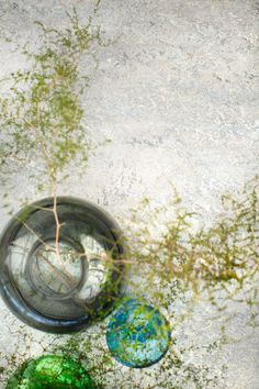 three different colored vases sitting on top of a cement floor next to green plants