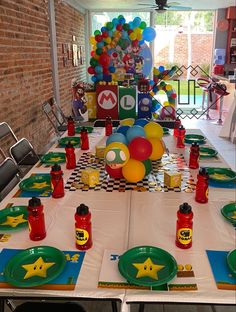 a table set up for a mario birthday party with balloons and soda cans on it