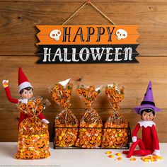 two elfs sitting next to each other in front of candy bags and halloween decorations