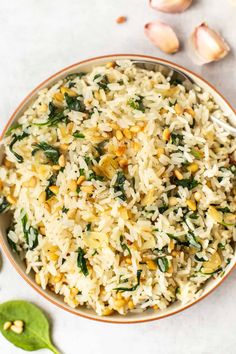 a bowl filled with rice and spinach on top of a white table next to garlic