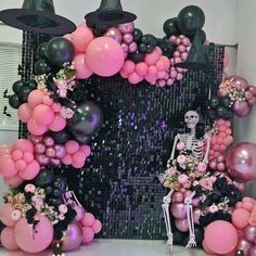 a skeleton sitting in front of a backdrop with balloons and flowers on the wall behind it