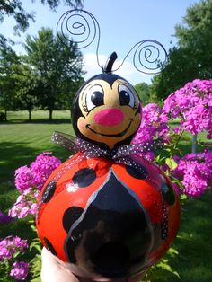 a ladybug decoration sitting on top of a hand in front of purple flowers