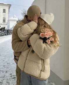 a man and woman hugging each other on a snowy day in front of a building