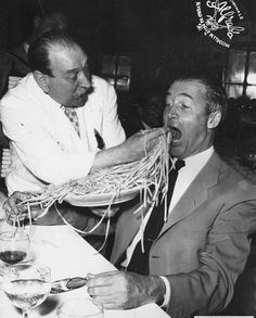 an old photo of two men at a table eating spaghetti off of their hands while another man looks on