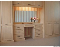 an empty dressing room with wooden cabinets and flowers in vases on the dresser top