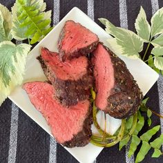 a white plate topped with meat next to green leafy plants on top of a table