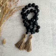 black beads with tassels are arranged on a white surface next to dried grass