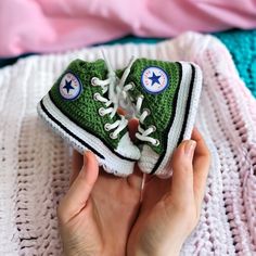 someone is holding up a crocheted green converse shoe